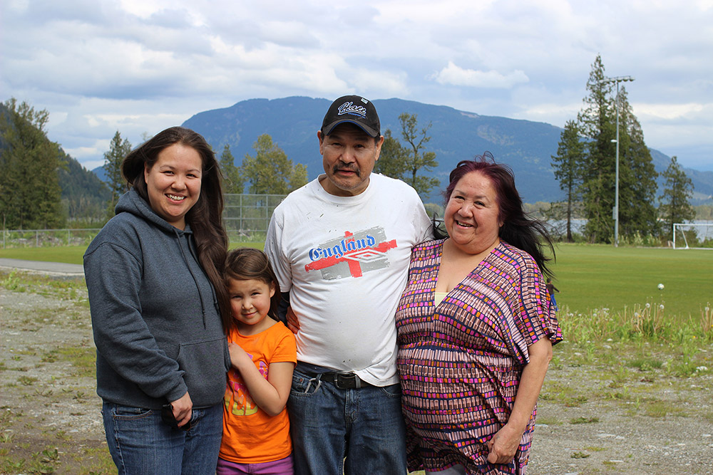 Two women, one man, and a young girl pose for a picture outside, with the trees and mountains behind them.