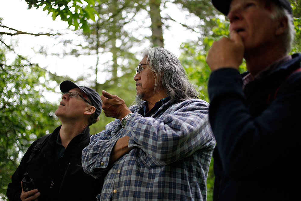 Three men standing and talking in a forested area.