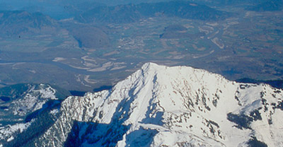 Vue aérienne d’une montagne au sommet enneigé et un paysage vert et montagneux à l’arrière-plan. 