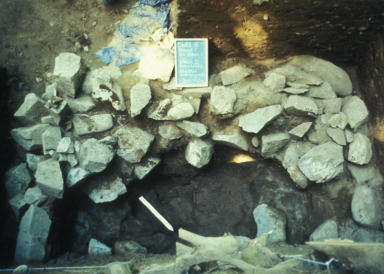 A rock formation is visible from inside an excavated archaeological mound.