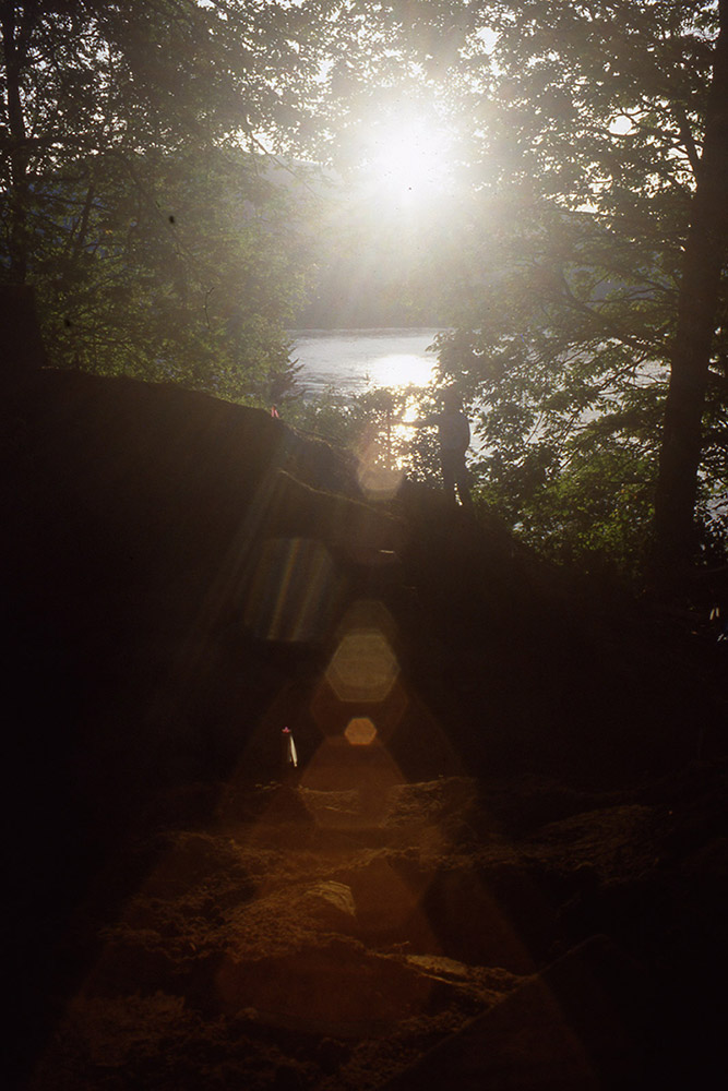 A view of the sun setting over a river with trees framing the foreground.