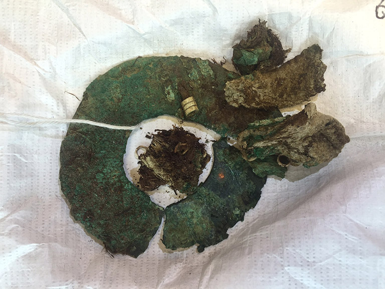 A large flattened oxidized metal hoop, with four four small pieces attached, greenish in color.