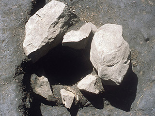Six light grey irregularly shaped boulders, lining a hole in the ground.
