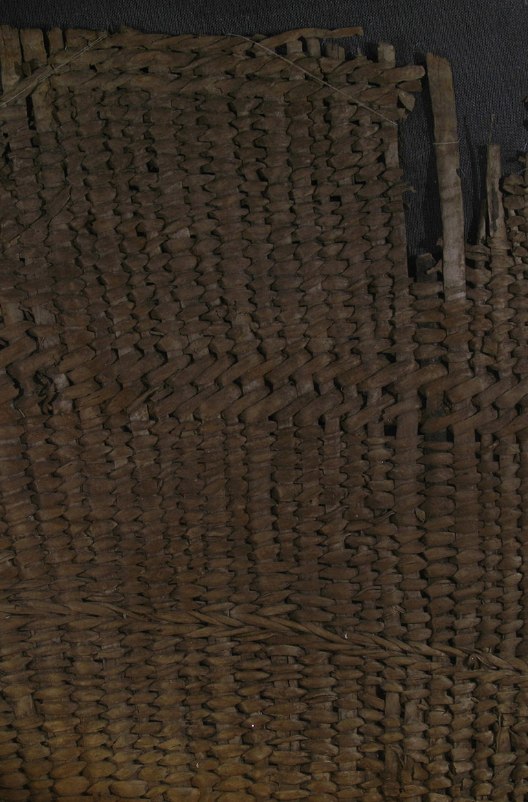 A fragment of woven basketry. The weaving material is brownish red.