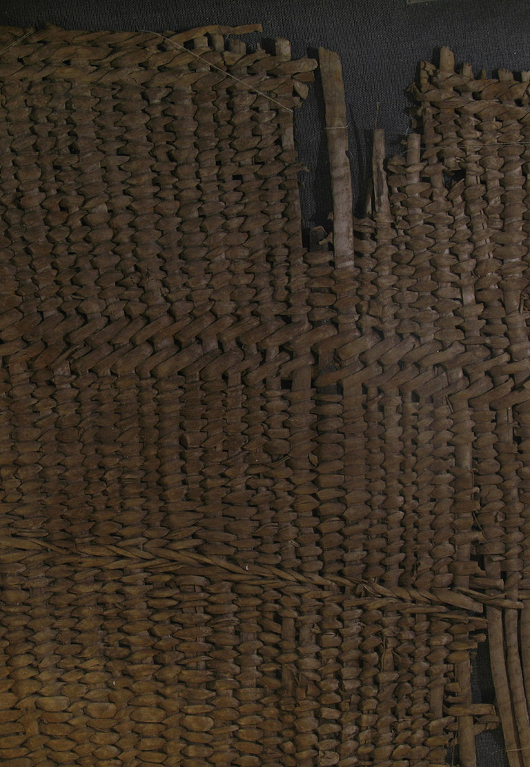 A fragment of woven basketry. The weaving material is brownish red.