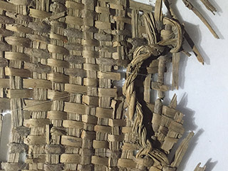 A close up view of the rim, body, and handle of a fragmented basket woven from bark strips.