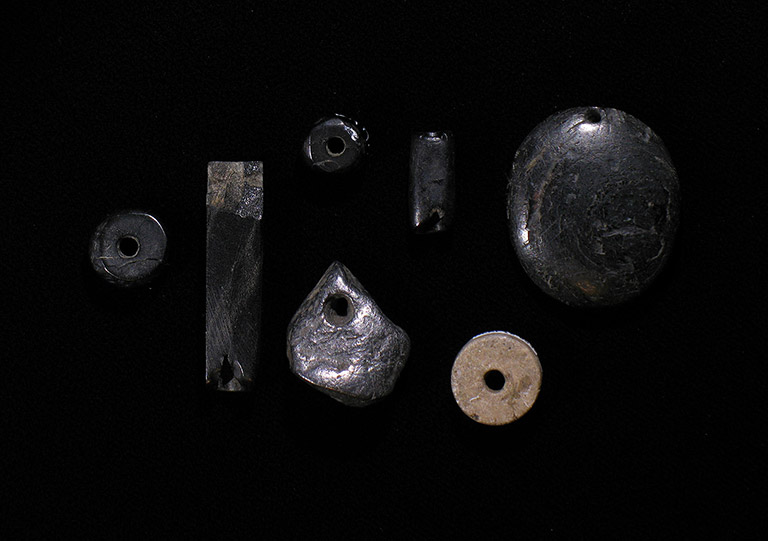 Sept perles et pendentifs de pierre de formes et de grosseurs différentes. Une des perles est pâle et les autres sont noires.