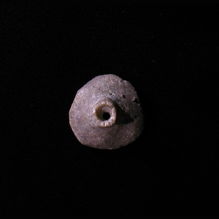 Le devant d’une pierre façonnée en demi-cercle avec un trou en saillie percé au centre.