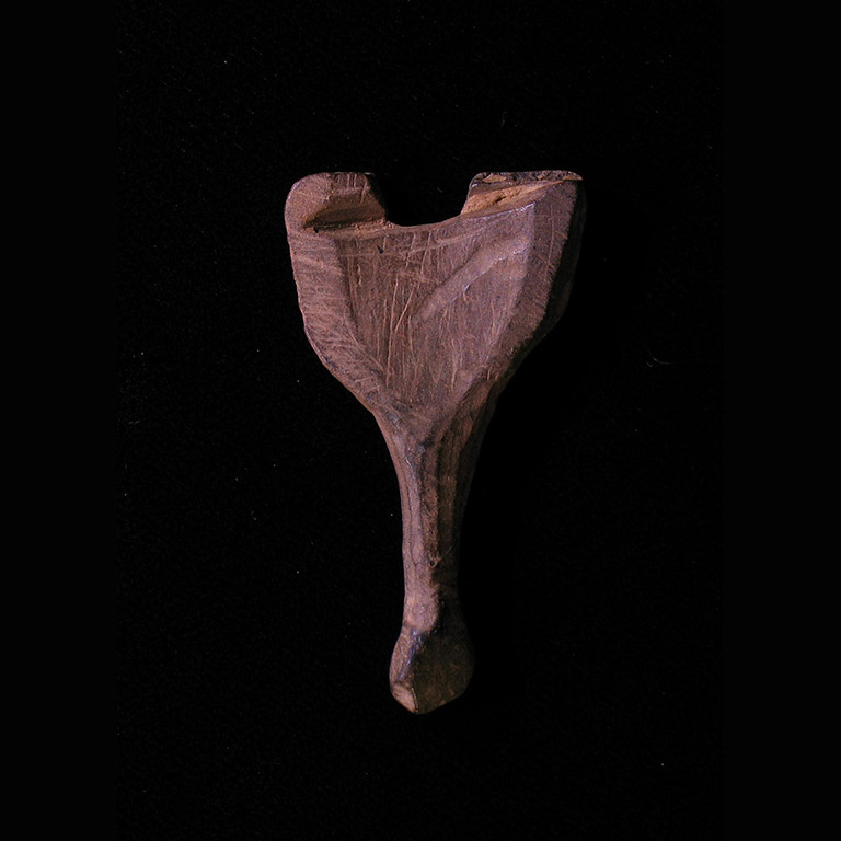 The back of a small carved figurine of a head, with a short handle descending from it.
