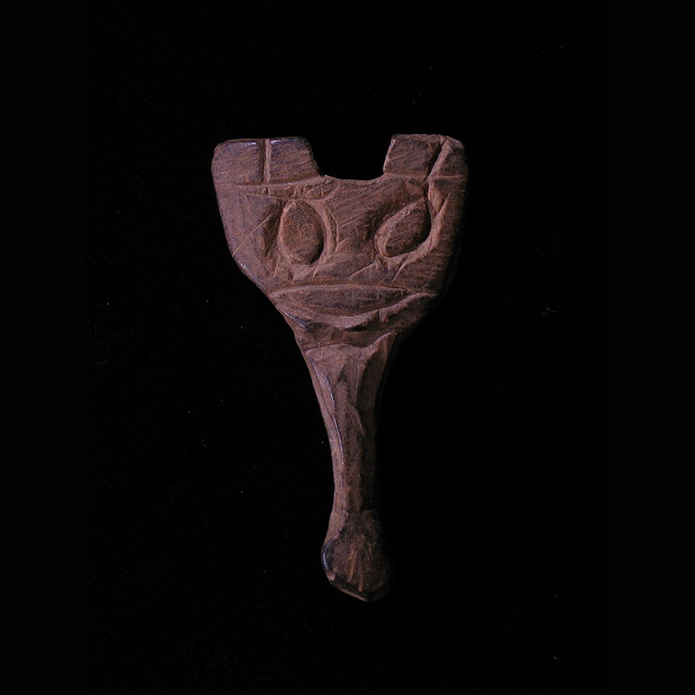 The front of a small carved figurine, with a face and a handle descending from it.