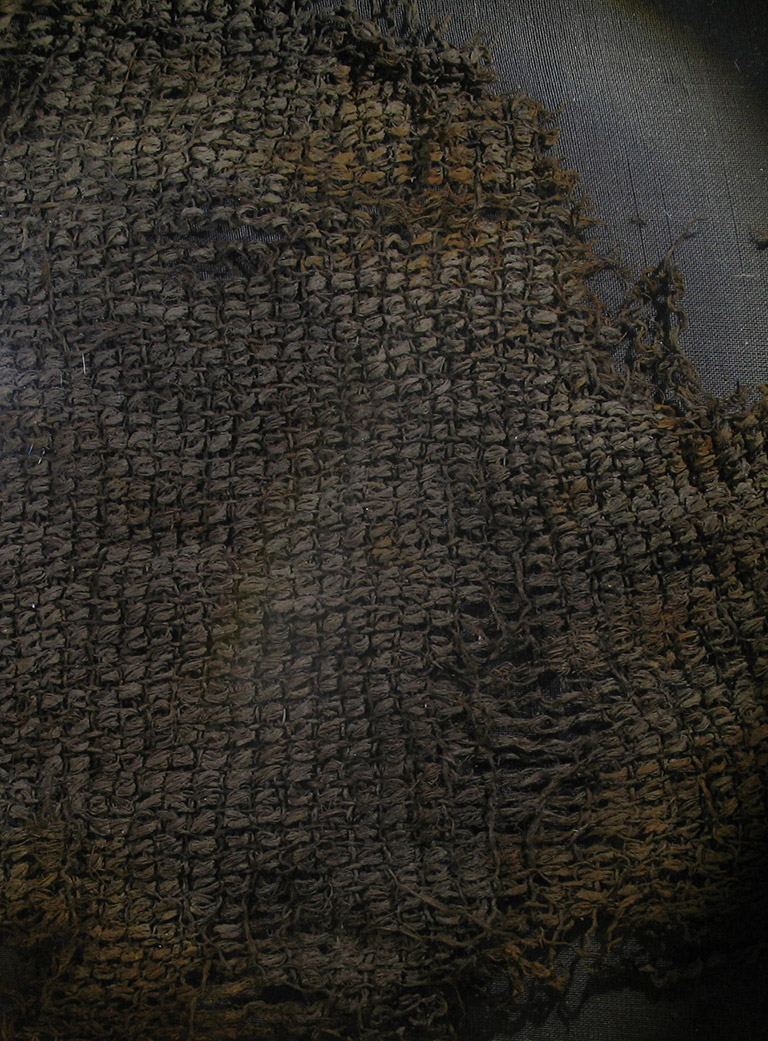 A fragment of tightly woven fabric, greyish in colour.