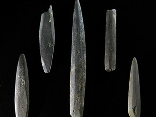 Cinq morceaux de pierre de forme étroite façonnés en pointes. Une des pointes est brisée et un des morceaux n’est pas taillé en pointe.