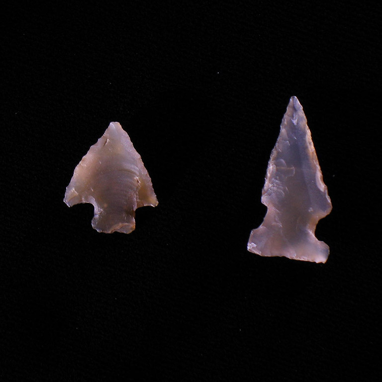 Two arrowheads made of translucent rock on a black background.