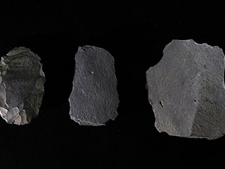 Three pieces of dark grey stone with sharp edges on a black background.