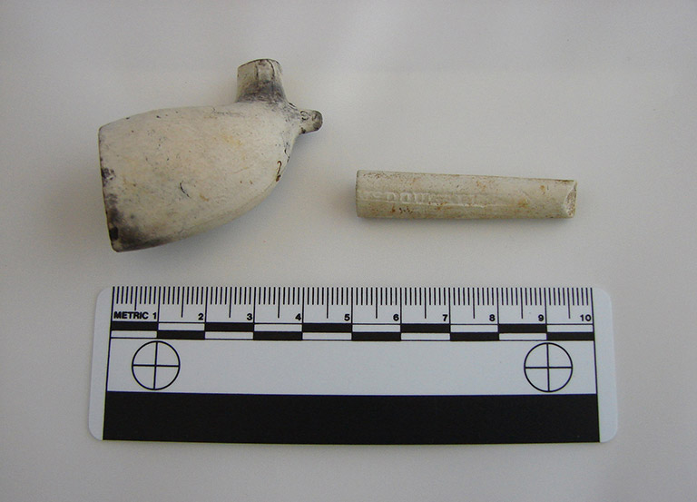 Smooth white hollow tube and smooth surfaced white hollowed cup that appear like pipe pieces.