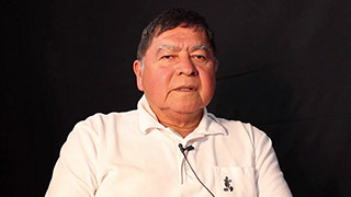 A man sits in front of a video camera, sharing his stories.
