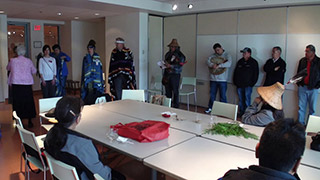 A group of elders and adults stand around a table with cedar branches.