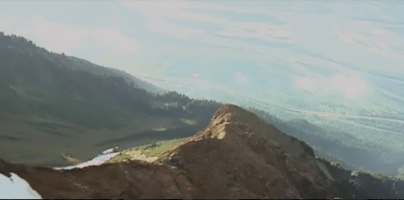 Vue aérienne du sommet d’une montagne. Elle est brune en grande partie avec des sections boisées plus bas et à l’arrière-plan.