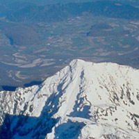 Vue aérienne d’une montagne au sommet enneigé et un paysage vert et montagneux à l’arrière-plan.